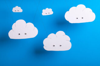 Cloud computing concept with white cardboard cutout cute clouds with eyes hanging in front of a sky blue background.