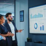 Company Operations Manager Holds Meeting Presentation. Diverse Team Uses TV Screen with Growth Analysis, Charts, Statistics and Data. People Work in Business Office.