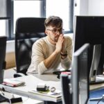 Programmer sitting at the desk in his office and trying to solve problem of new code.