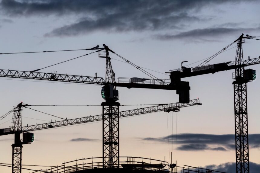 a set of construction cranes against the sunset