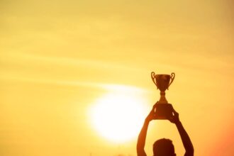 Winner holding golden trophy cup above head sun and golden sky in background