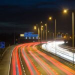 Smart motorway in England, UK with light trails signifying busy traffic at rush hour. The NSL symbols under the gantry sign signify an end to speed restrictions.