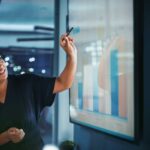 Company Operations Director Holds Sales Meeting Presentation for Employees and Executives. Creative Black Female Uses TV Screen with Growth Analysis, Charts, Ad Revenue. Work in Business Office.