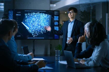 In the Conference Room Chief Engineer Presents to a Board of Scientists New Revolutionary Approach for Developing Artificial Intelligence and Neural Networks. Wall TV Shows Their Achievements.