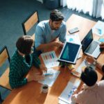 Top view of business people discuss idea while marketing team joining meeting. Manager pointing financial graph while colleagues talking to investor by using phone and brainstorm idea. Convocation.