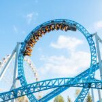 upside down roller coaster in a loop against a cloud and blue sky amusement park