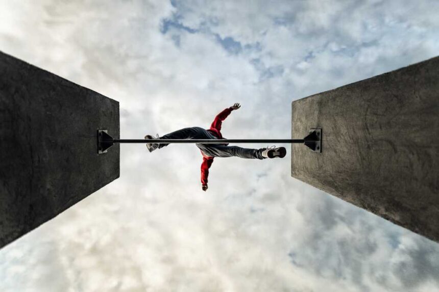 man jumps over obstacle, parkour leaps across gap, view from below looking up at cloud filled sky