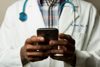 Doctor on a smartphone illustrating the AI Airlock scheme from the Medicines and Healthcare products Regulatory Agency (MHRA) in the UK that aims to accelerate the adoption of artificial intelligence technologies into the NHS healthcare system with a high emphasis on safety.