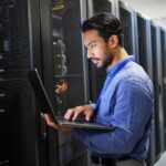 Programming, data center and a man with a laptop for maintenance, cyber security and internet check. Coding, email and an Asian programmer typing on a computer for network or server analytics