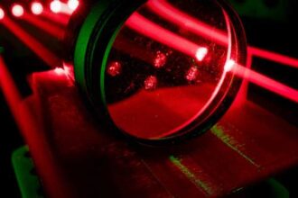 Experiment with red laser using prism in optics lab. Streaming red light and lens against a black background.