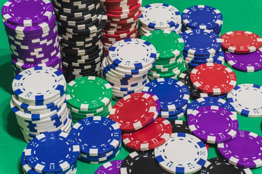 stacks of red white blue green black purple casino chips or betting chips on green gambling or gaming table