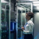Medium shot of female technician working on a tablet in a data center full of rack servers running diagnostics and maintenance on the system