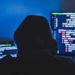 Computer hacker silhouette of hooded, man using laptop and monitor for steal data. Cyber crime concept.