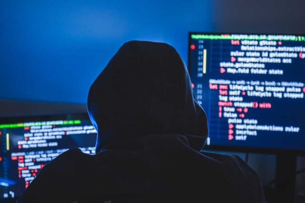 Computer hacker silhouette of hooded, man using laptop and monitor for steal data. Cyber crime concept.