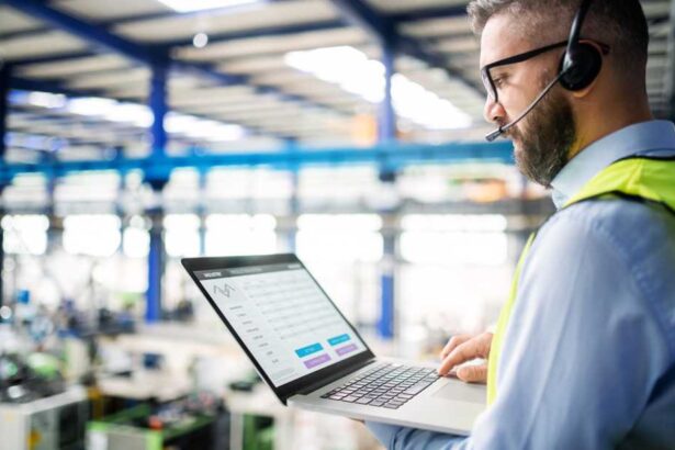 Side view of technician or engineer with headset and laptop standing in industrial factory.
